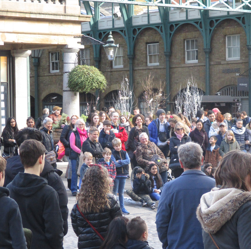 Spectators watching the street entertainers outside Covent Garden market hall in London